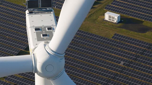 Aerial view of a wind turbine towering over a solar panel array, creating a striking contrast of textures and tones, Middelharnis, South Holland, Netherlands.