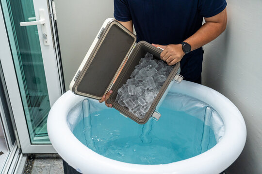 Pouring ice cubes into inflatable tub for ice bathing, practicing cold therapy and Wim Hof Method for wellness meditation fitness recovery and sports therapy.