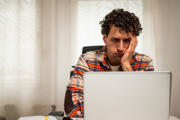 Worried and overworked businessman using laptop while working from his home.	