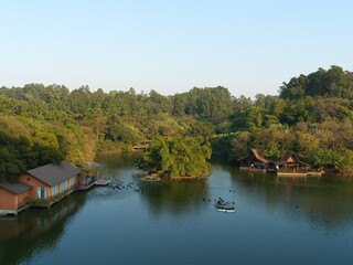 Obraz premium Aerial view of a serene lake surrounded by lush greenery and traditional-style buildings with a small boat on the water