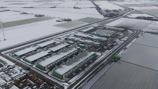 Aerial view of a sprawling Agriport datacenters complex, dusted with snow, contrasts sharply with the dark rooftops and the reflective greenhouses, Middenmeer, North Holland, Netherlands.