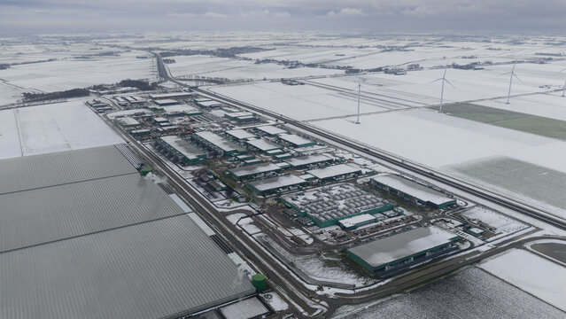 Aerial view of a sprawling data center complex, the buildings' green roofs contrasting with the crisp white snow dusting the surrounding fields, Middenmeer, North Holland, Netherlands.
