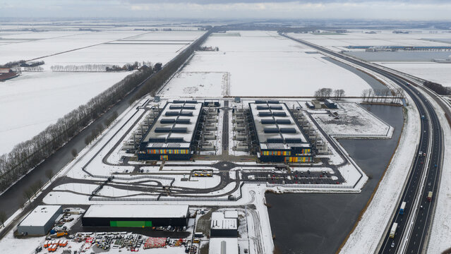 Aerial view of modern buildings with colorful accents amidst a snow-covered landscape, bordered by a highway and canals, Middenmeer, North Holland, Netherlands.