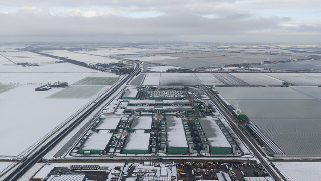 Aerial view of a vast, snow-dusted landscape punctuated by the geometric shapes of data centers, their green roofs contrasting with the white fields, Middenmeer, North Holland, Netherlands.