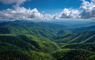 Fototapeta premium Aerial perspective of lush, forested mountain ranges under a vibrant blue sky filled with fluffy white clouds