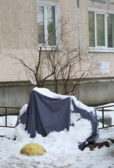 A motorcycle covered with a cover and covered with snow is parked near a residential building