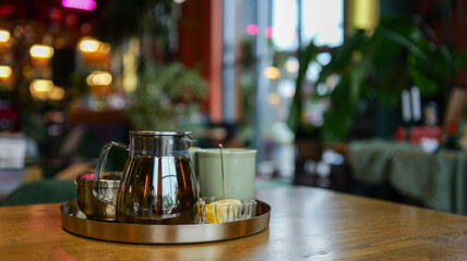 Elegant glass teapot with tea and lemon slices on a round tray in a cozy cafe