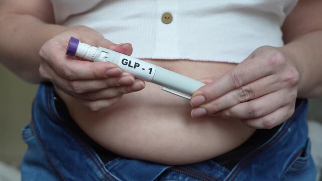 Woman holding GLP-1 injection pen, preparing to administer medication to her abdomen, showcasing the pen's components and her midsection in a home setting