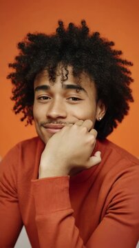 Close-up portrait of a young man with curly hair and a gentle smile, resting his chin on his hand