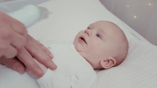 Careful father's hands gently using a nasal aspirator to clear a cute infant's stuffy nose, helping the newborn breathe easier while lying on a soft white changing pad