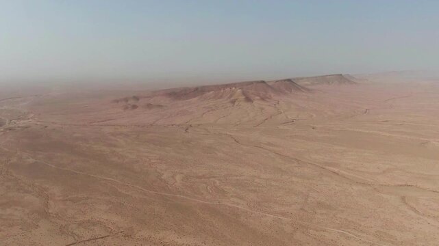 Aerial drone footage showing a vast arid desert plateau with rocky formations erosion patterns and immense scale emphasizing isolation geology and natural landforms