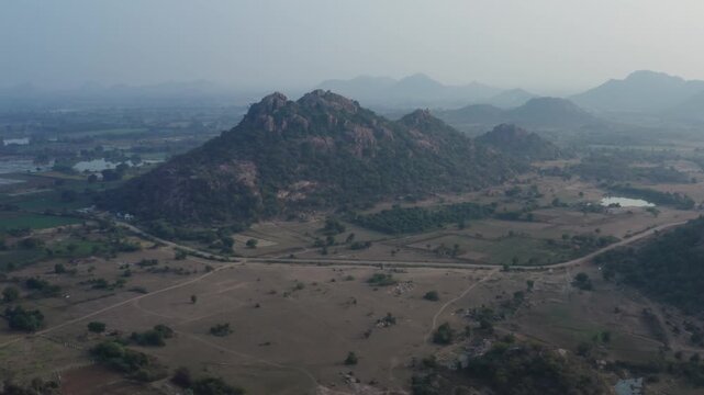 A cinematic drone journey rising above the lush agricultural fields and rugged Deccan Plateau terrain of rural Warangal, Telangana, showcasing the region's natural beauty and traditional village outsk