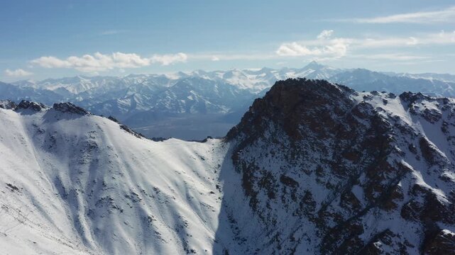 Sideways moving aerial view of snow covered mountain ridges with the Stok Kangri range in the distance, showing dramatic Himalayan altitude, winter terrain, and remote wilderness.