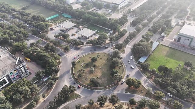 Aerial view of a landscaped roundabout in Greater Noida, where tree-lined roads intersect around a circular green island, highlighting planned infrastructure and smooth urban traffic flow.
