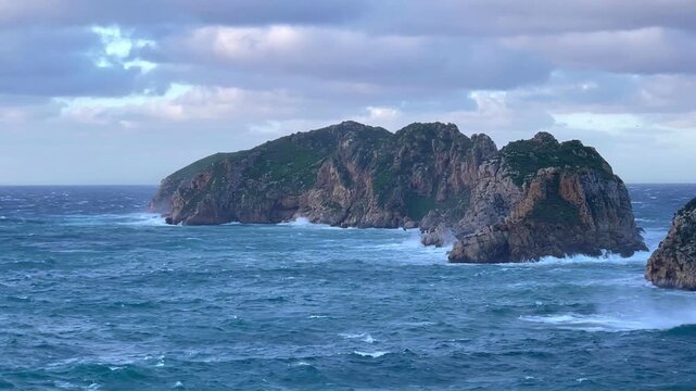 A stormy Mediterranean Sea after dawn. Storm waves crash against the base of a rocky island. Video slow motion 0.9x. Island of Mallorca, Spain.