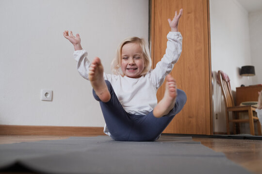 Little girl practicing yoga in Boat Pose Navasana on a mat.