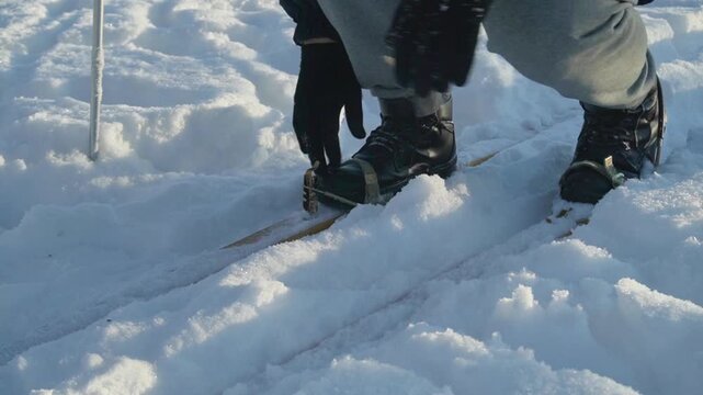 Individual prepares for skiing by adjusting bindings on skis while standing in deep snow under bright sunlight in a winter landscape