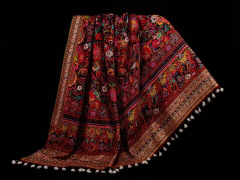 Colorful traditional floral textile with intricate patterns and tassels, draped on a black background. Rich ethnic fabric with ornamental details.