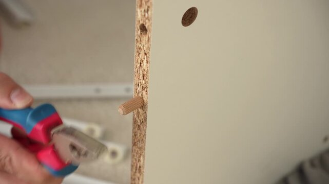 Hand inserting wooden dowel into furniture panel during indoor repair task.