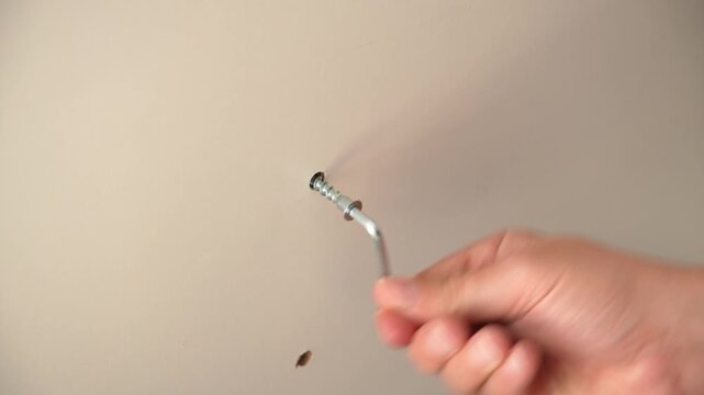 Hand unscrewing wall fastener indoors during home maintenance repair.