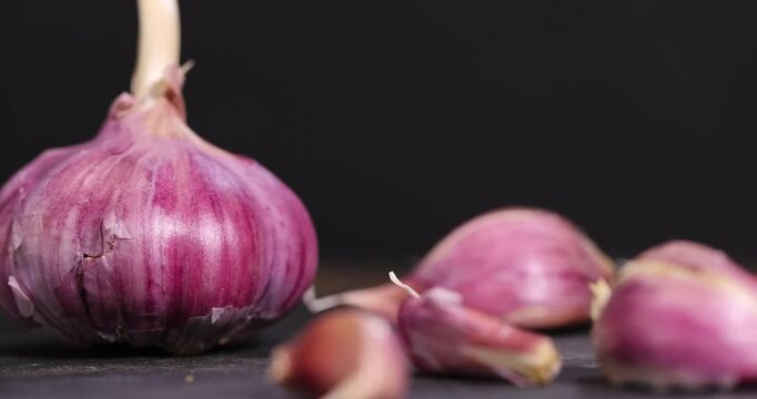 purple garlic scattered on a black table in the kitchen and cloves of crushed garlic , garlic spices lie on a black slate board in the kitchen over cooking