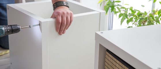 Extra wide DIY furniture assembly process with cordless drill, handyman installing flat pack cabinet, home improvement renovation banner with copy space