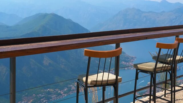 Scenic mountain viewpoint bar overlooking kotor bay. Empty bar chairs on a sunny observation deck offering a breathtaking panoramic view of the majestic mountains and the blue waters of the bay