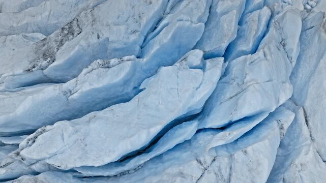 Close aerial view of cracked blue ice at Briksdalsbreen glacier in Norway. Detailed crevasses and frozen textures create an abstract natural pattern in summer light.