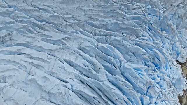 Wide close-up view of Briksdalsbreen glacier ice in Norway. Aerial footage reveals layered blue ice patterns and deep crevasses shaped by slow glacier movement.