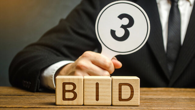 Businessman Holding Bid Paddle With 'BID' Wooden Blocks