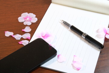 日本の春のイメージ：机の上に置かれた便箋、万年筆、スマホ、桜の花びら(横長)
