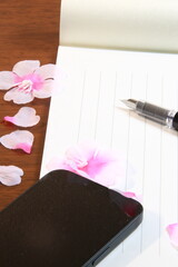 日本の春のイメージ：机の上に置かれた便箋、万年筆、スマホ、桜の花びら(縦長)