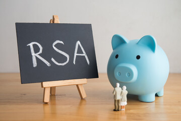 Senior couple looking at RSA (retirement savings account) text writing on blackboard with blue piggy bank on wooden table. Financial planning for elder, money risk management and so on concept.