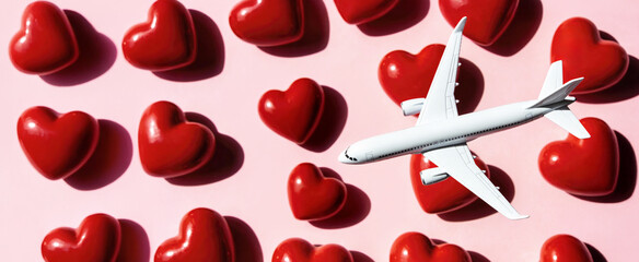 Airplane flies above red heart shapes scattered on a pink surface, representing themes of love and travel, suitable for Valentine's Day promotions