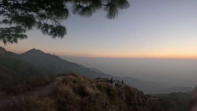 Panoramic POV view of a mountain valley at twilight with a visible moon, mobile tower, and distant silhouettes of hikers on a windy path.