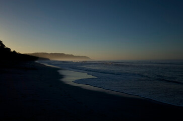 Obraz premium Serene tropical beach at dawn with misty mountains and gentle waves
