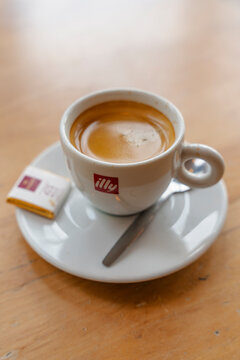 January 23, 2026, Amsterdam, Netherlands - A cup of Illy espresso with a spoon and chocolate on a saucer on a wooden table