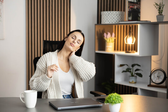 A woman gently stretches her neck in a stylish office chair, promoting relaxation and comfort amid work.