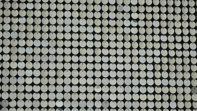 Reflective circular pattern. Metallic, reflective, circular discs, sequins or reflective panels, arranged in a grid pattern.