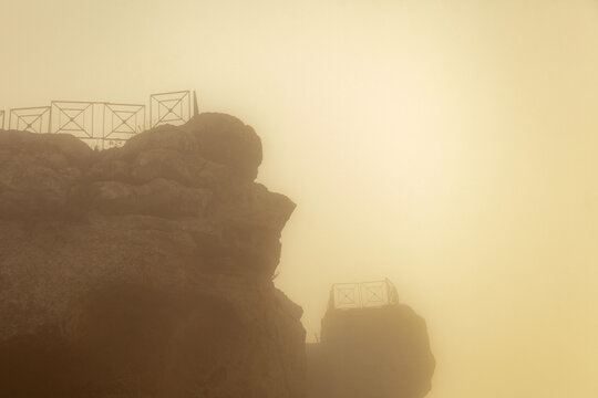 Rocca di Cerere rock formation shrouded in mist with viewing platforms visible against a hazy background in Enna, Sicily, Italy