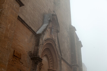 Historic stone church facade in Enna, Sicily, Italy, partially obscured by fog, showcasing intricate architectural details and weathered textures