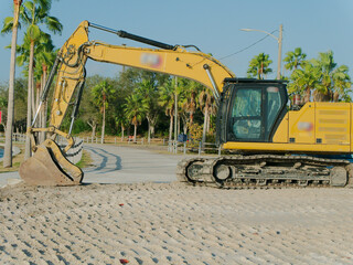 Yellow Excavator On Sandy Beach By Palm Trees Along Waterfront Construction Scene in Gulfport, FL. A large yellow excavator sits on a calm waterway in the background. Perfect for stock imagery of cons © Del Harper