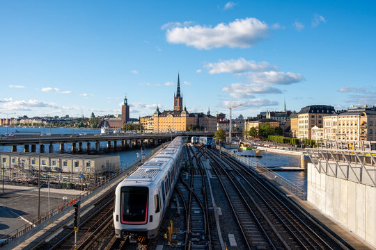Stockholm Sweden train on railway tracks approach toward urban skyline and horizon delivering fast transport connection in clear daylight