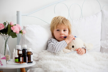Fototapeta premium Sick little blond toddler boy, lying in bed with fever, hugging little fluffy toy, medicine next to him
