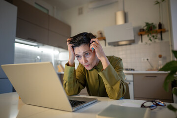 Overworked worried senior woman freelancer working on laptop late at home, sitting staring at...