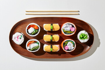 Set of paper sushi on a wooden plate over white background. Top view with copy space. Pure and fresh concept and composition.