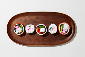 Set of paper sushi on a wooden plate over white background. Top view with copy space. Pure and fresh concept and composition.