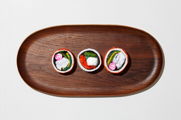 Set of paper sushi on a wooden plate over white background. Top view with copy space. Pure and fresh concept and composition.