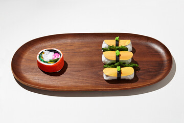 Set of paper sushi on a wooden plate over white background. Top view with copy space. Pure and fresh concept and composition.