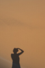 Portrait of a female photographer capturing her own shadow projected on the ochre sand of the Namib Desert dunes